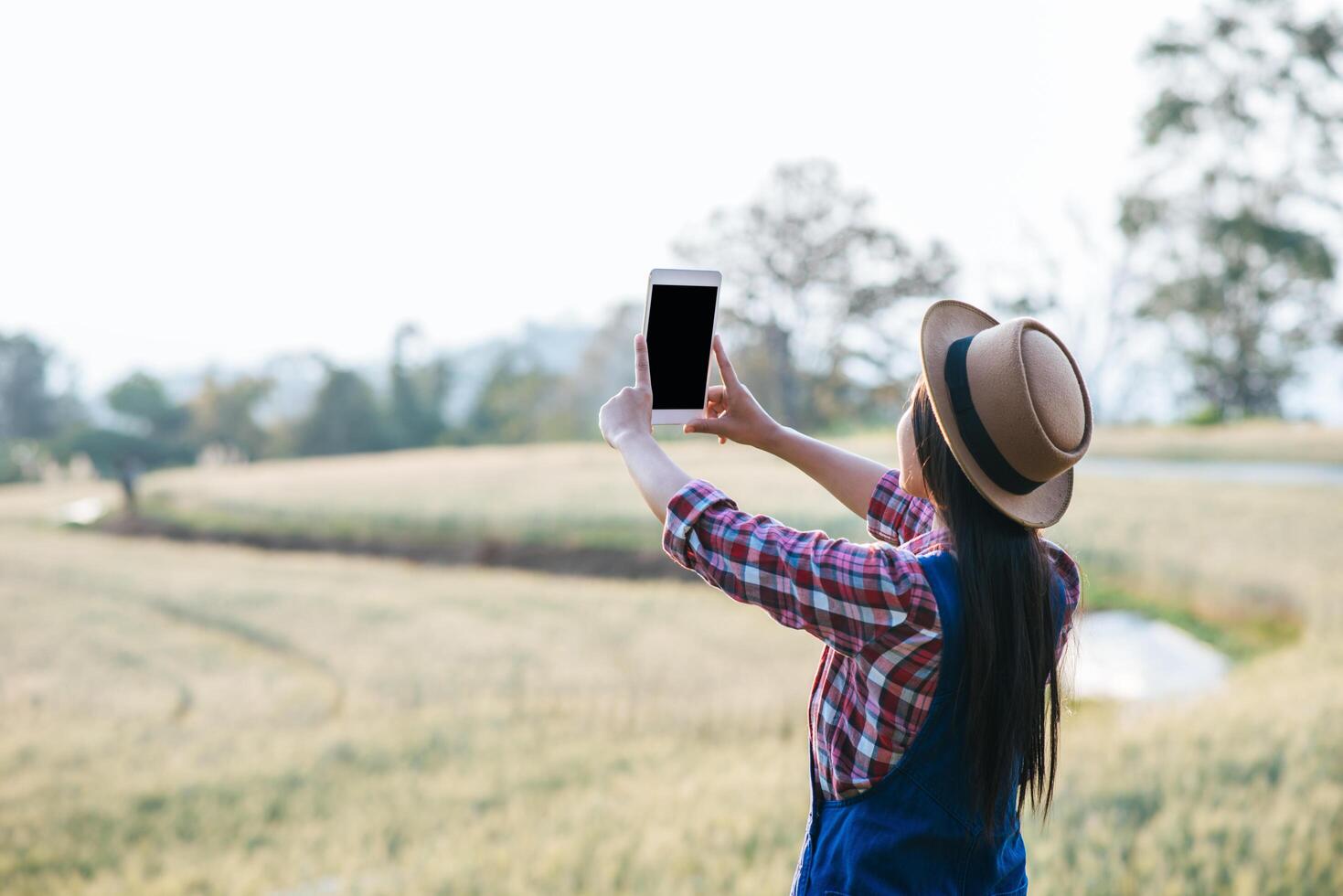 Intelligente Bäuerin, die mit Telefon auf Gerstenfeld schaut foto