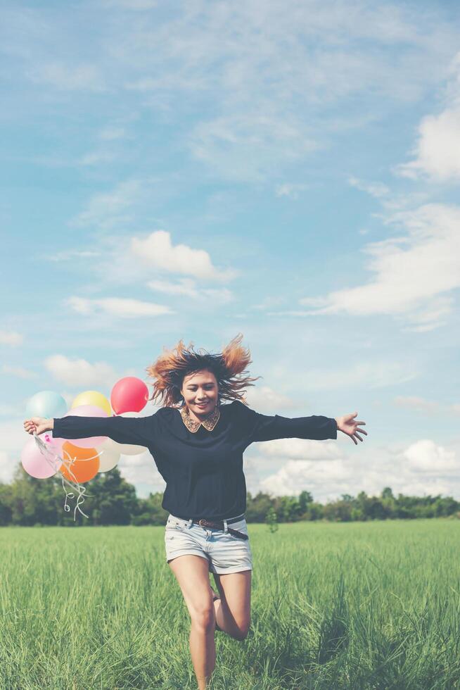 junge Frau mit Ballon auf grünem Grasland läuft und frische Luft genießt foto