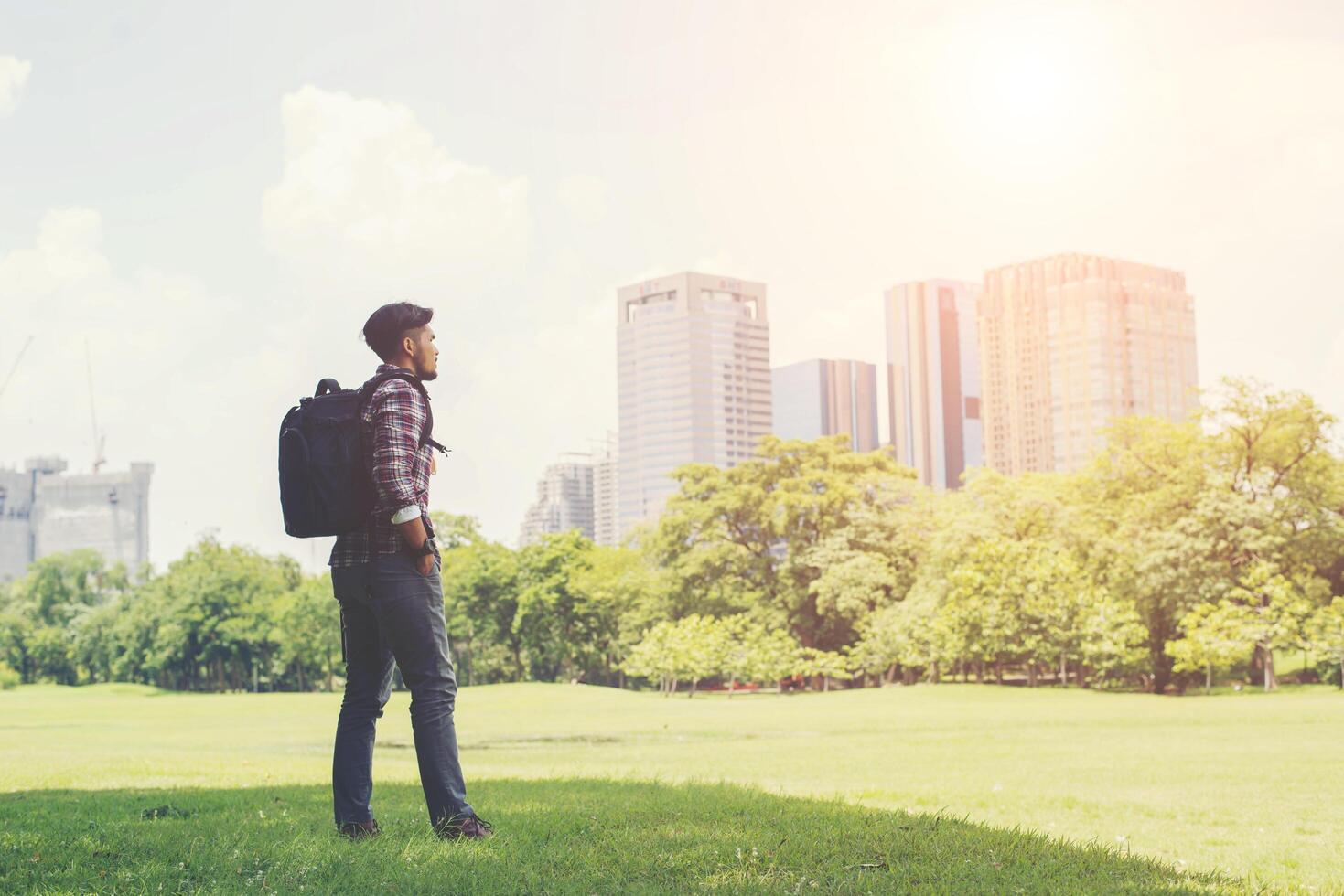 Der junge Hipster-Mann genießt auf Reisen den Blick auf die Stadt vom Park aus foto