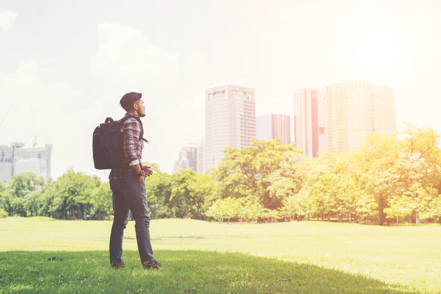 Der junge Hipster-Mann genießt auf Reisen den Blick auf die Stadt vom Park aus foto