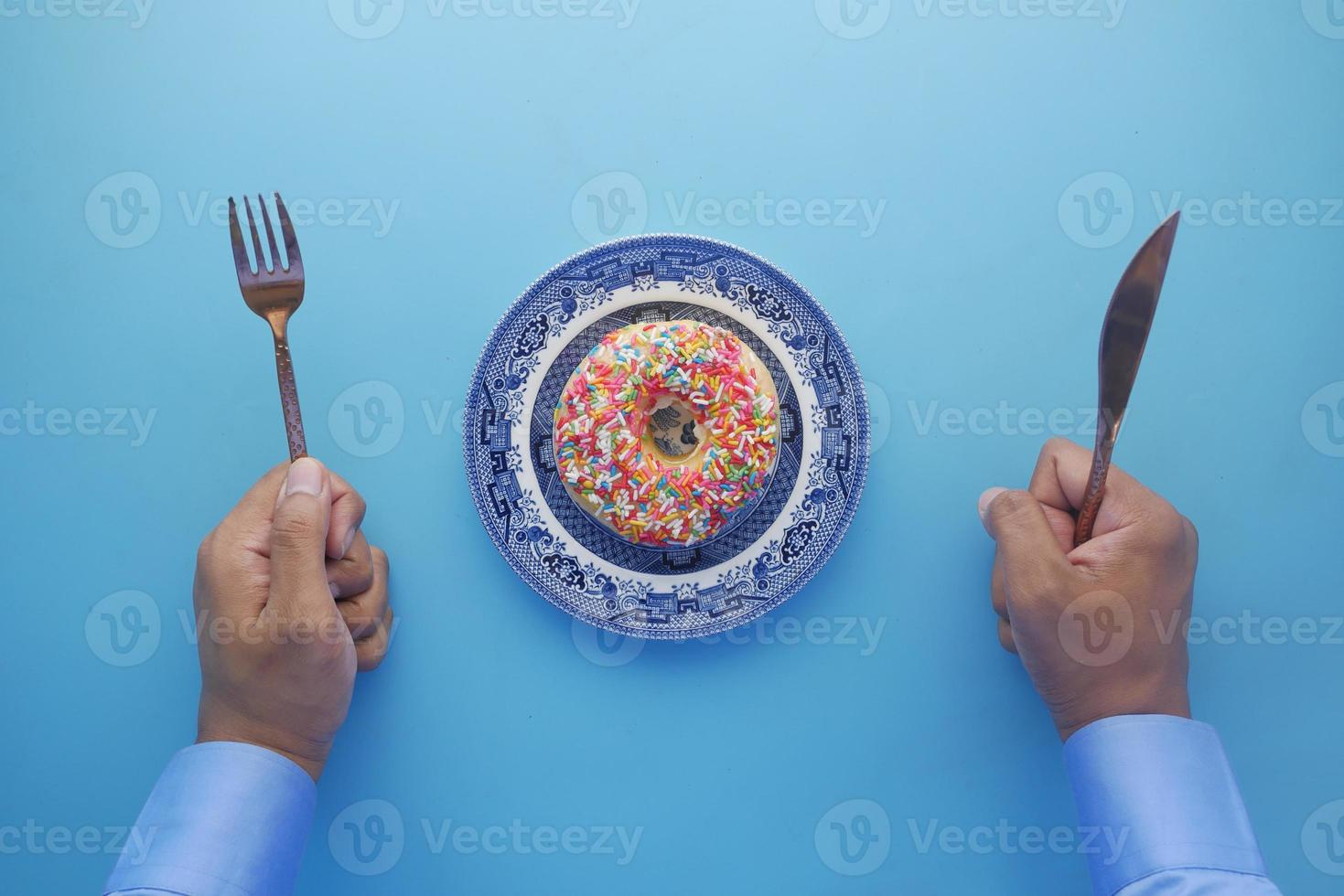 Blick von oben auf die Hand des Mannes mit Messer und Gabel zum Essen von Donuts? foto