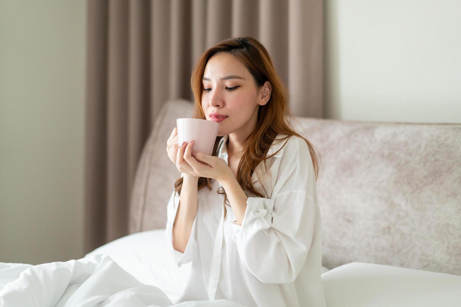 Porträt schöne asiatische Frau wacht auf und hält morgens eine Kaffeetasse oder einen Becher auf dem Bett foto