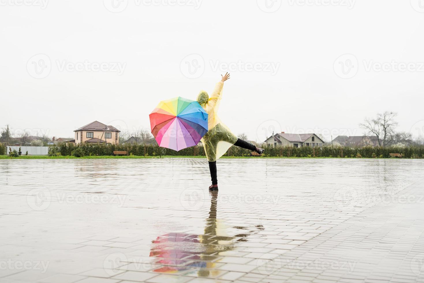 schöne brünette frau mit buntem regenschirm tanzt im regen foto