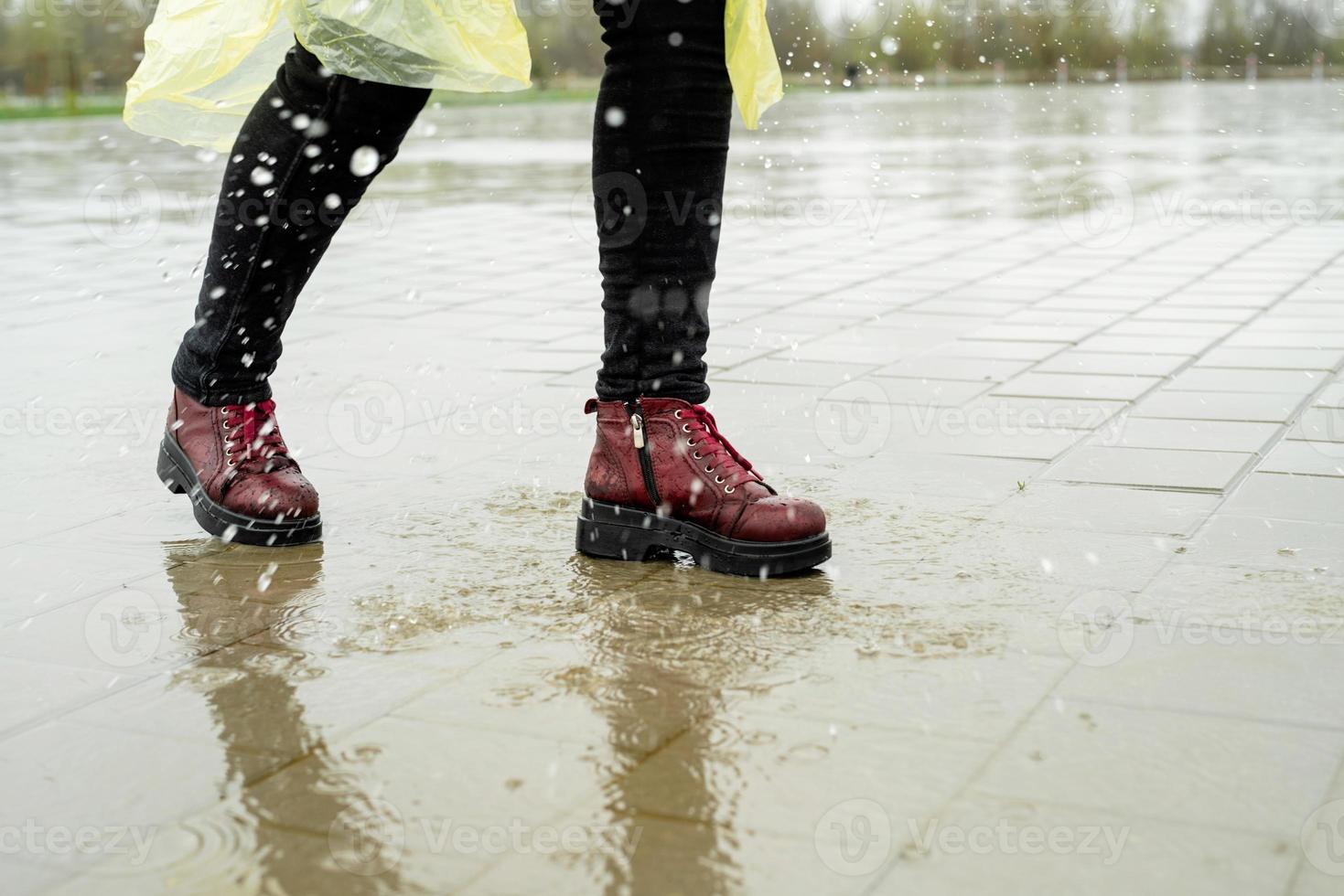 Frau, die im Regen spielt, mit Spritzern in Pfützen springt foto