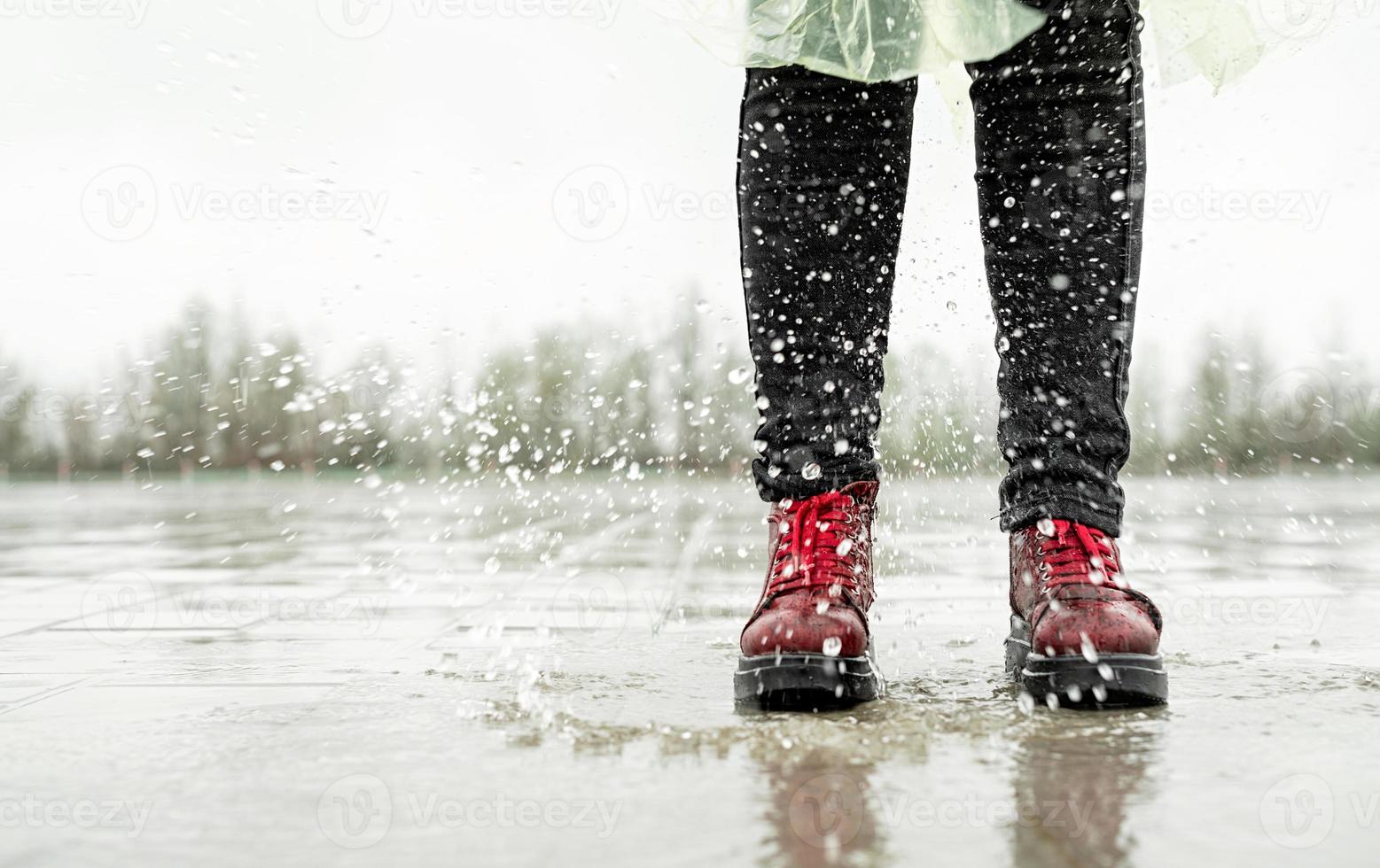 Frau, die im Regen spielt, mit Spritzern in Pfützen springt foto