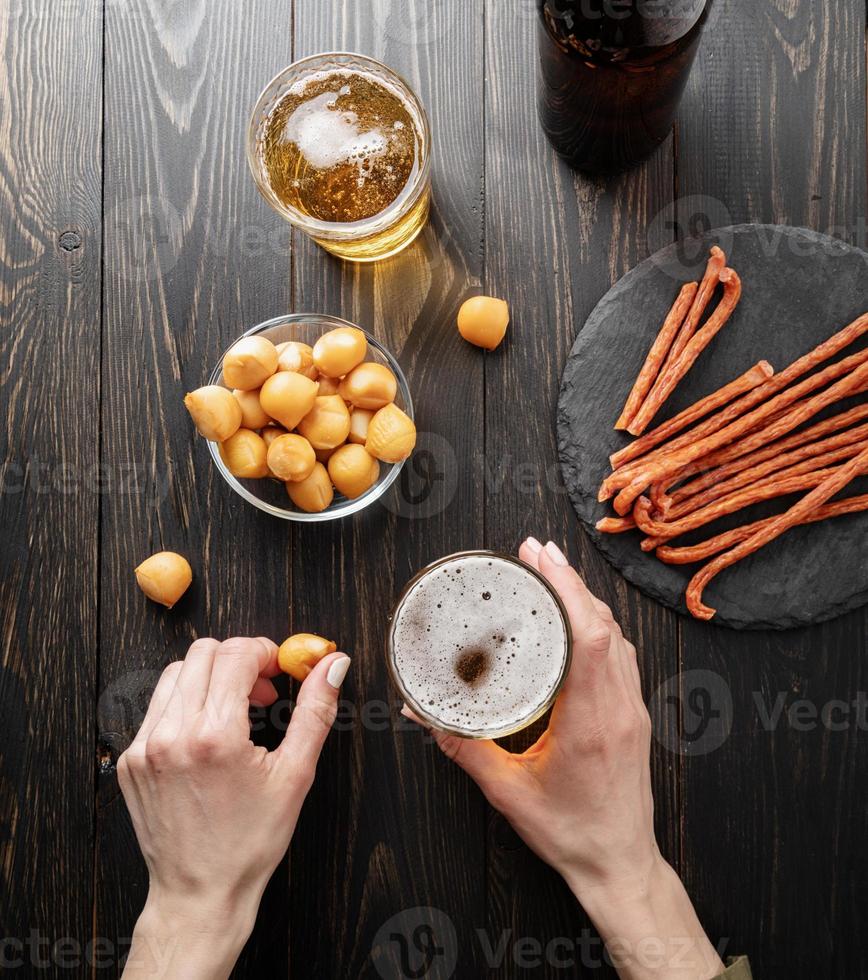 Frauenhände halten ein Glas Bier und Käsesnack auf schwarzem Hintergrund foto