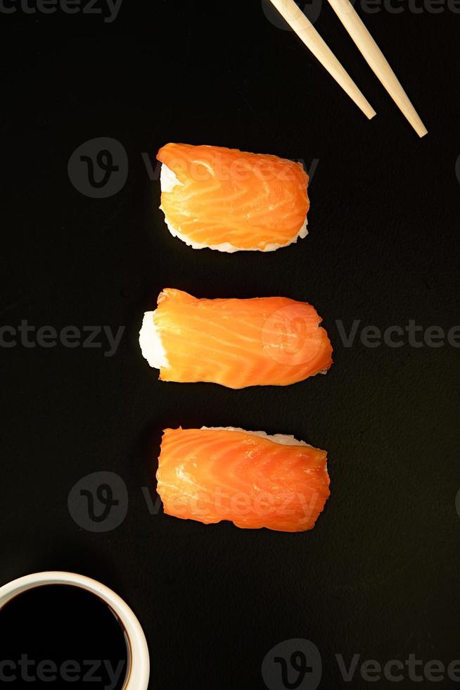 Sushi mit Lachs und Stäbchen auf schwarzem Hintergrund isoliert foto