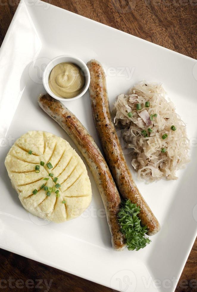 Deutsche Thüringer Bratwurst mit Kartoffelpüree und Sauerkrautmehl auf weißem Teller foto