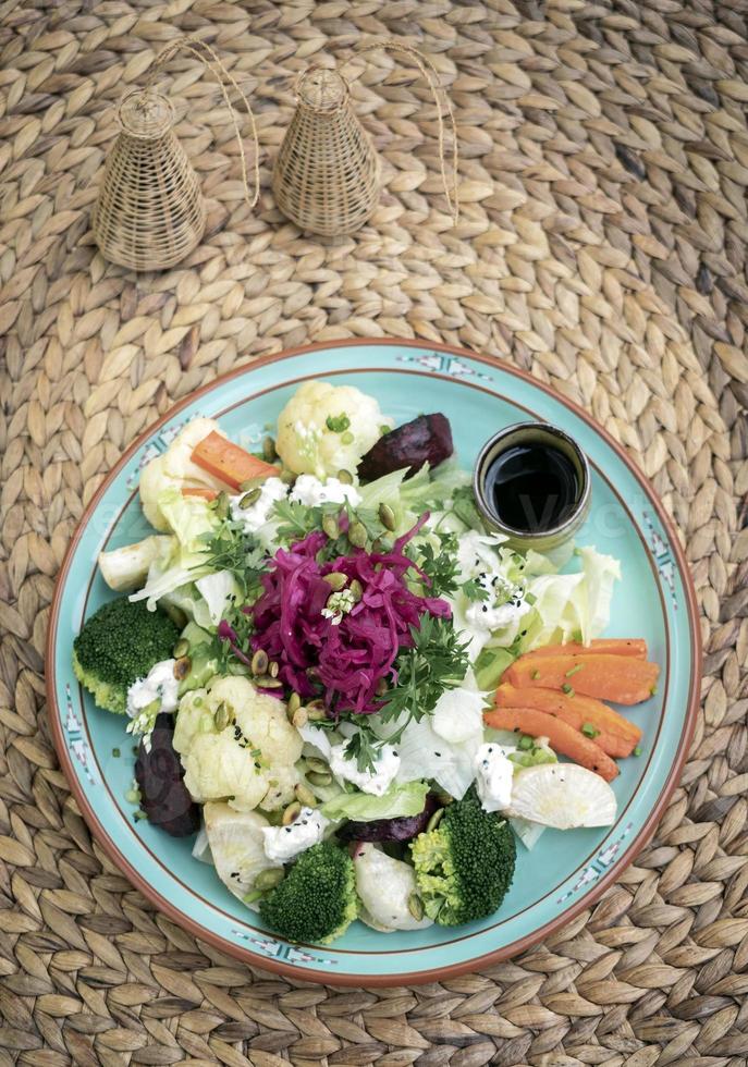 rustikaler Hüttensalat mit gesundem gemischtem gedämpftem und frischem Gemüse auf buntem Teller draußen im Garten foto