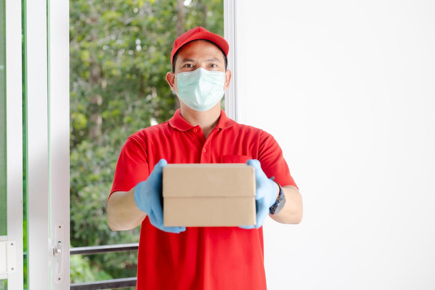 ein Zusteller mit rotem Hemd und Hut hält einen Paketkasten foto