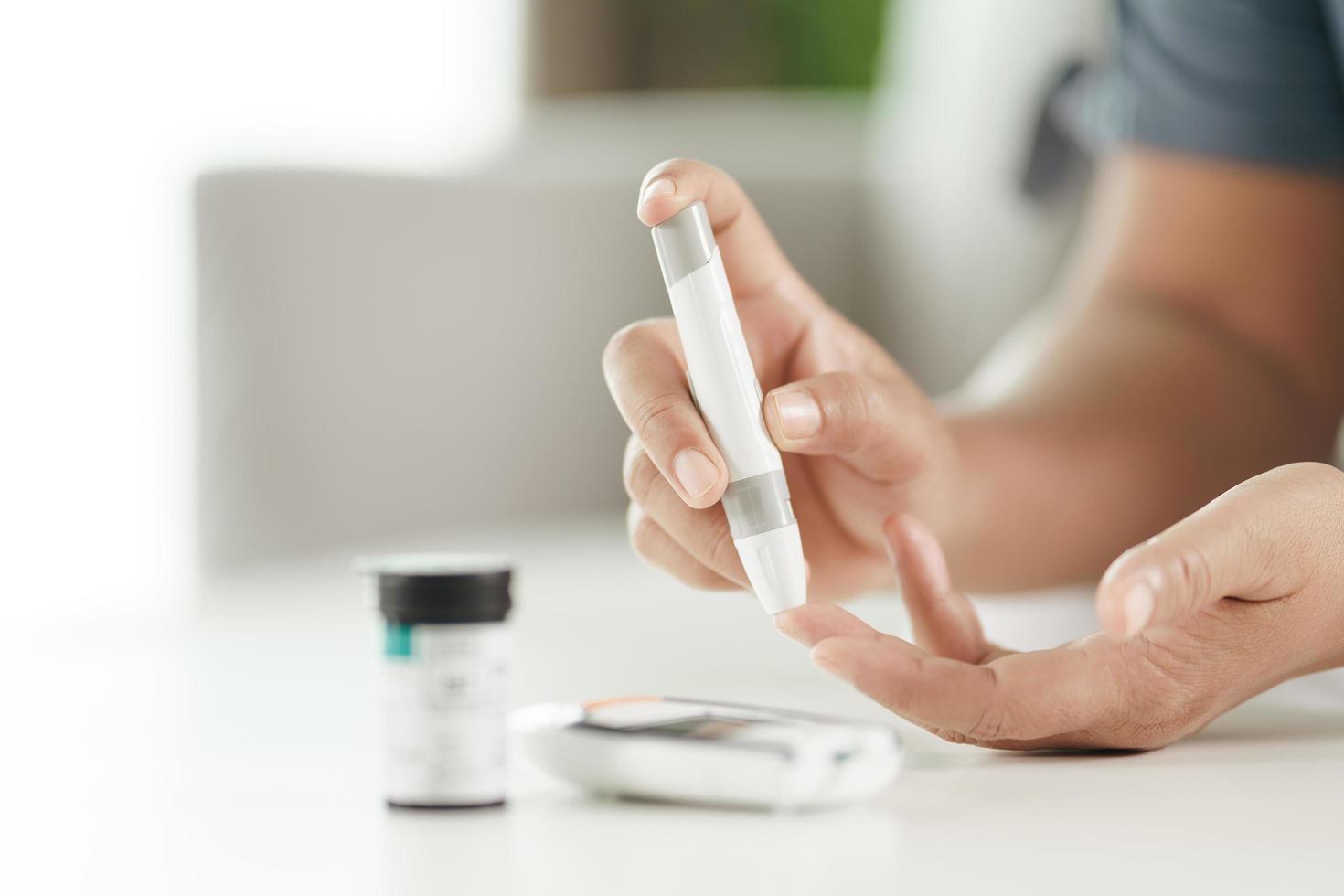 Frau verwendet Lanzette am Finger, um den Blutzuckerspiegel mit einem Glukosemeter zu überprüfen foto