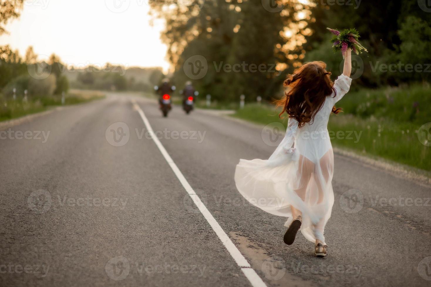 Rückansicht einer jungen Frau in einem weißen Kleid, die auf der Landstraße läuft foto