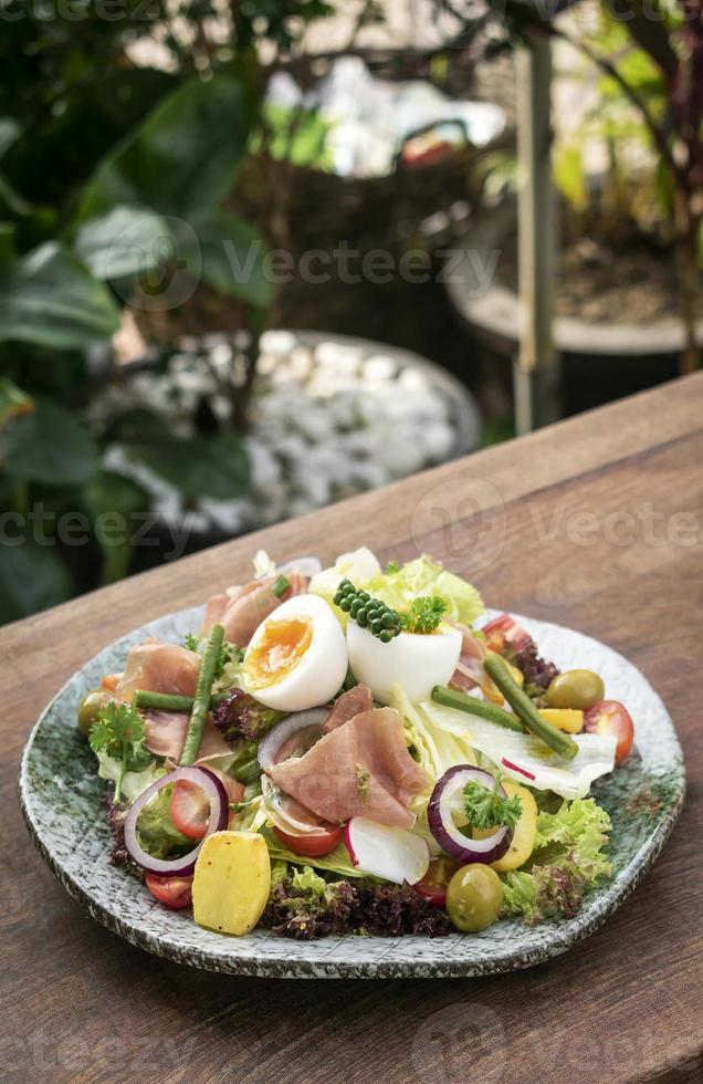 gesunder rustikaler Bio-Salat nach Nicoise-Art mit Ei und Schinken im Freien foto