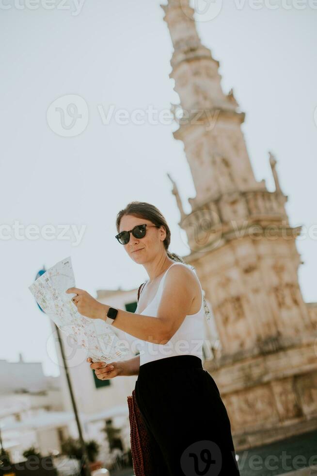 weiblich Tourist mit Stadt Karte durch das Heilige oronzo Statue im Ostuni, Italien foto