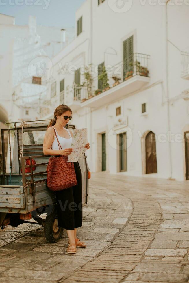 weiblich Tourist mit Papier Stadt Karte auf eng Straßen von Ostuni, Italien foto