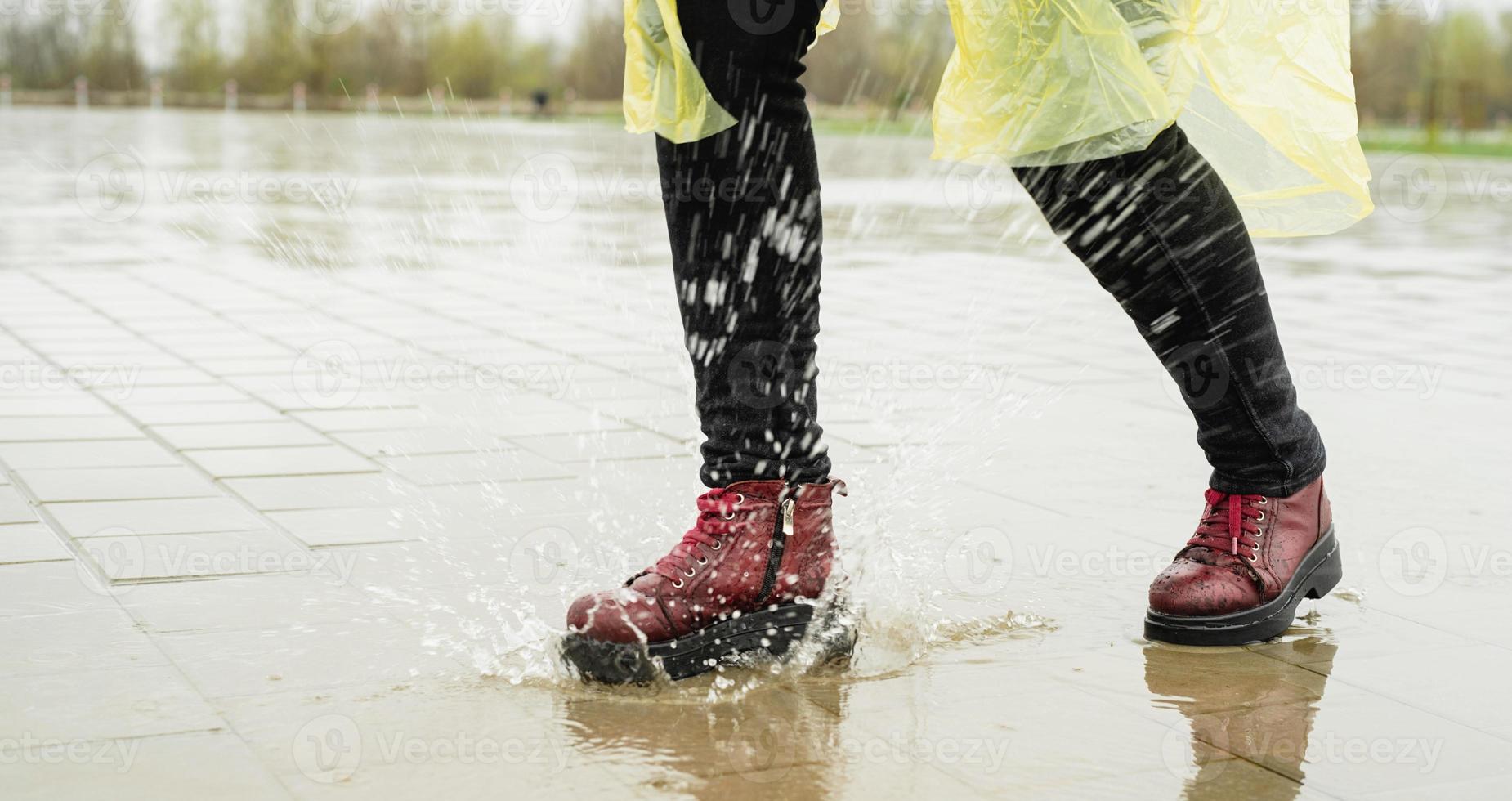 Frau, die im Regen spielt, mit Spritzern in Pfützen springt foto