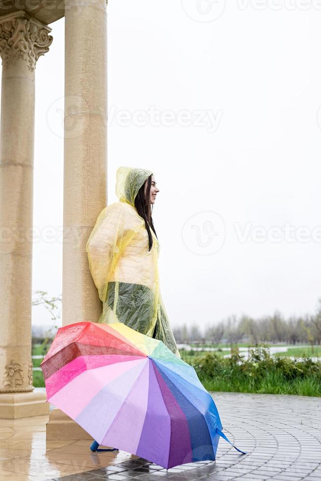 schöne brünette frau im gelben regenmantel, die draußen regen fängt foto