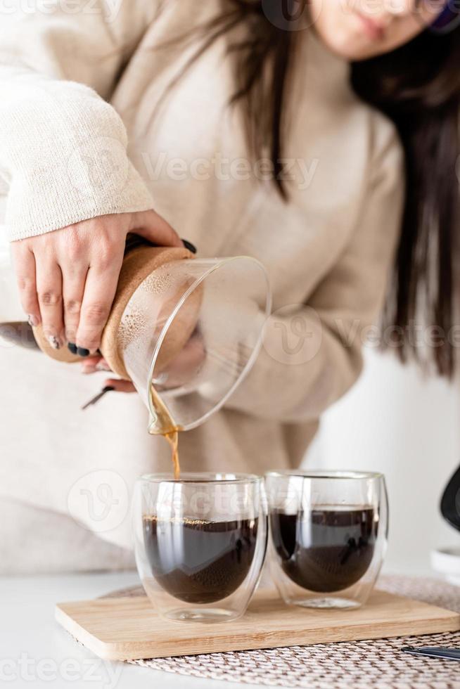 junge Frau, die Kaffee in der Kaffeekanne brüht, Kaffee in das Glas gießt foto