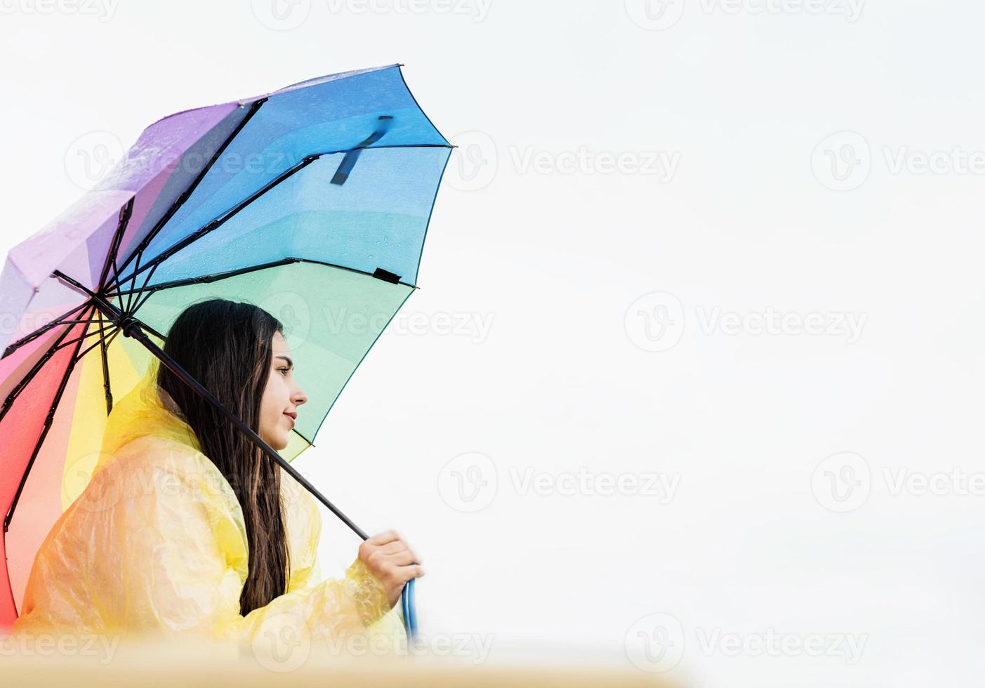 Frau, die draußen steht und einen regenbogenfarbenen Regenschirm hält foto