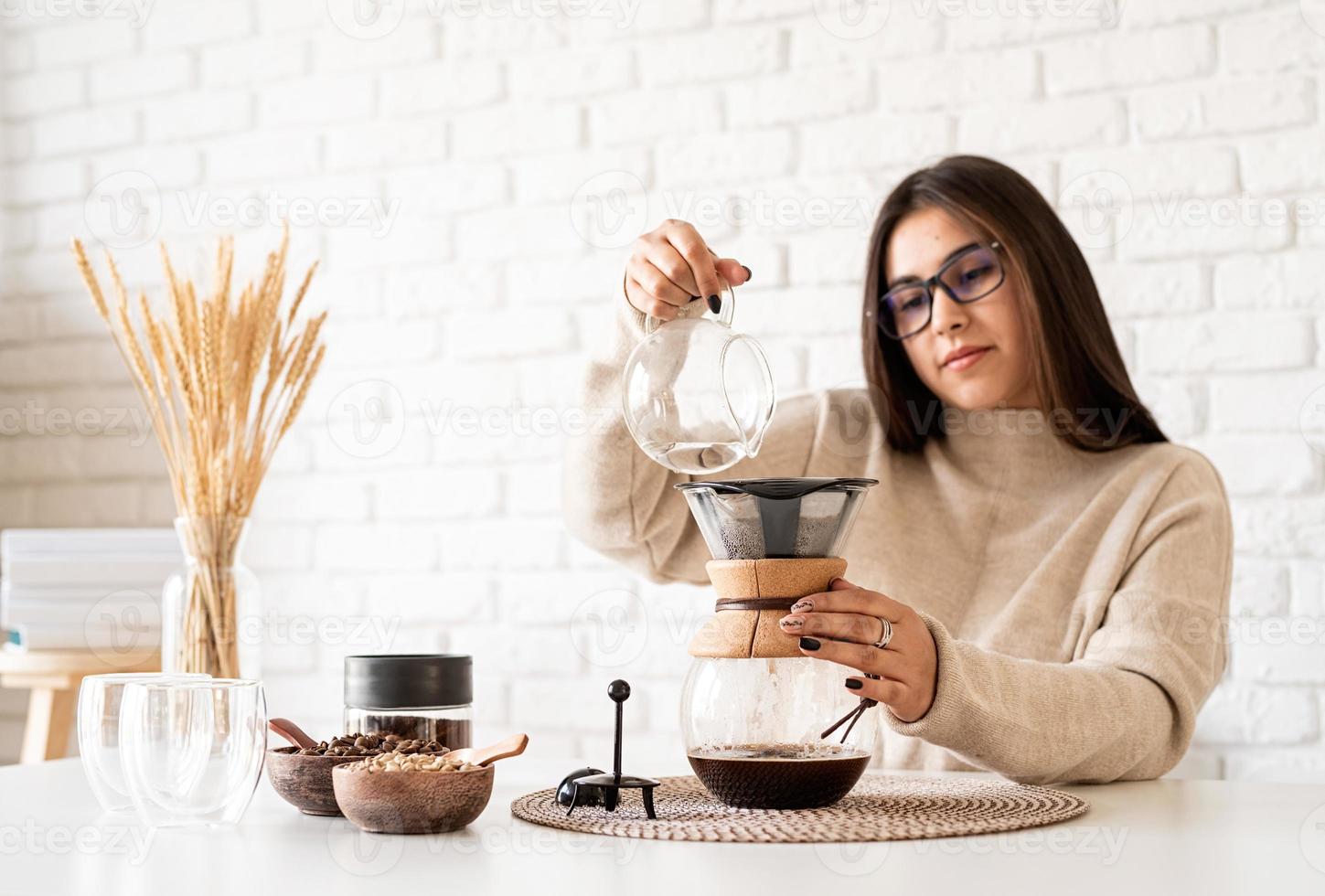 Frau, die Kaffee in der Kaffeekanne brüht und heißes Wasser in den Filter gießt foto