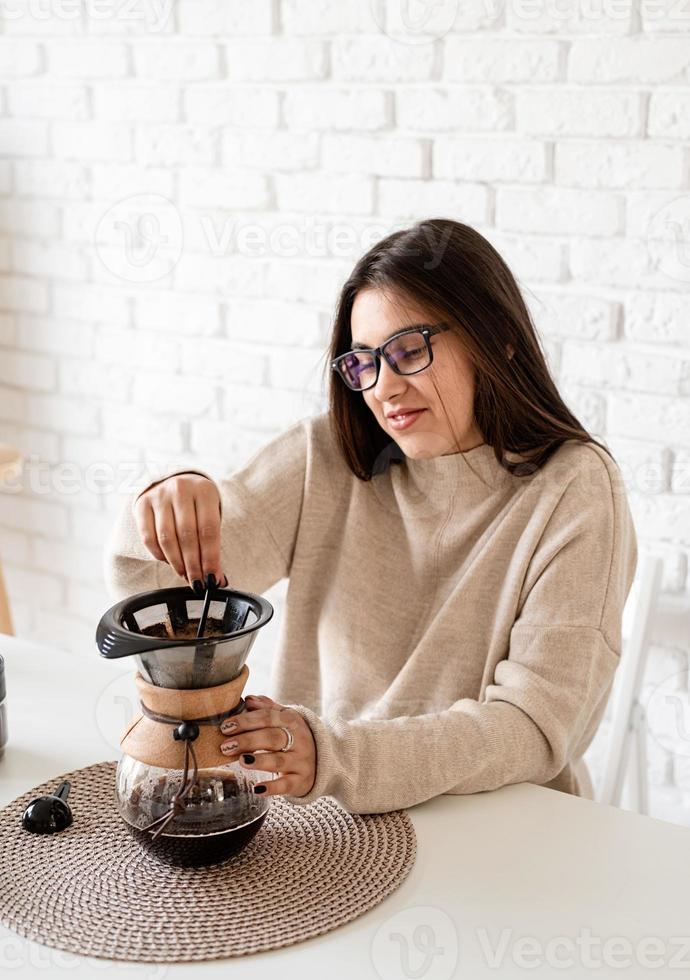 Frau, die Kaffee in der Kaffeekanne brüht und heißes Wasser in den Filter gießt foto