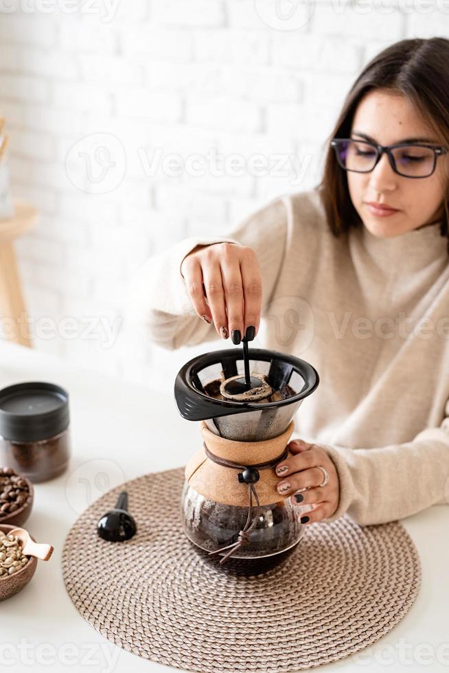 Frau, die Kaffee in der Kaffeekanne brüht und heißes Wasser in den Filter gießt foto