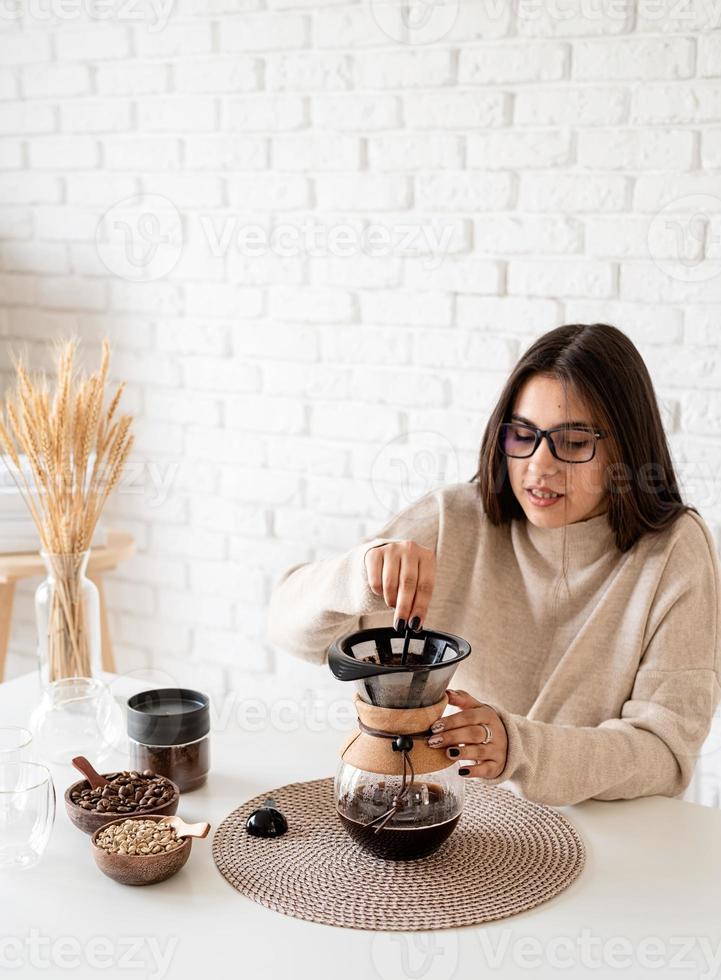 Frau, die Kaffee in der Kaffeekanne brüht und heißes Wasser in den Filter gießt foto