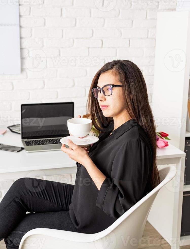 Frau, die im Büro arbeitet und Tee oder Kaffee trinkt foto