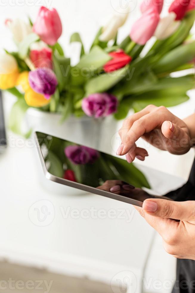 Frau arbeitet an digitaler Tablette, Eimer mit frischen Tulpen im Hintergrund foto