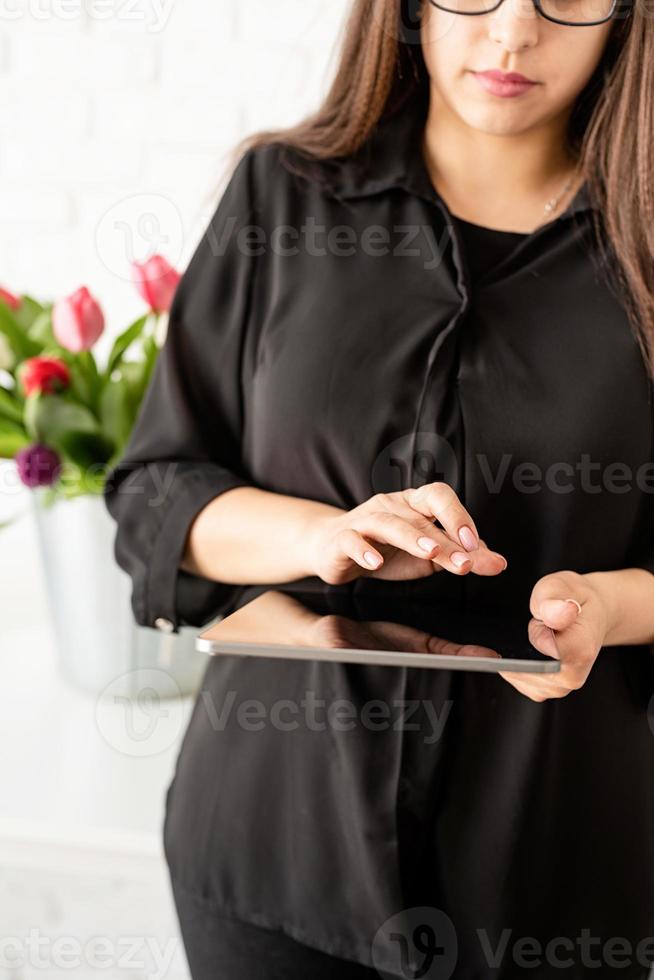 Frau arbeitet an digitaler Tablette, Eimer mit frischen Tulpen im Hintergrund foto