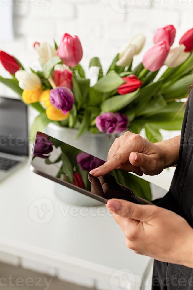 Frau arbeitet an digitaler Tablette, Eimer mit frischen Tulpen im Hintergrund foto