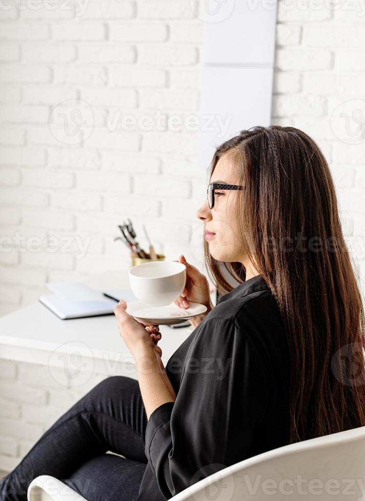 Geschäftsfrau, die im Büro arbeitet und Tee oder Kaffee trinkt foto