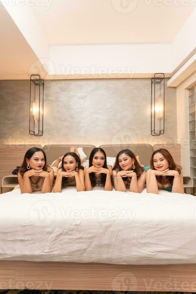ein Gruppe von asiatisch Frauen sind Lügen auf Weiß Matratzen mit ihr freunde im ein Hotel foto