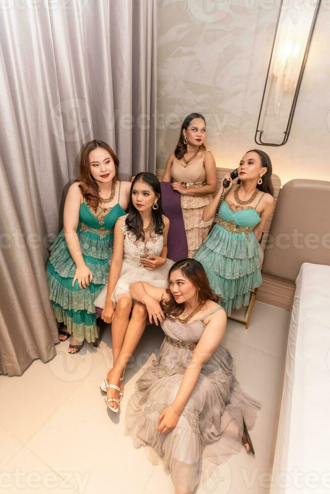 ein Gruppe von asiatisch Frauen im glamourös und luxuriös Kleider sind Sitzung auf das Sofa mit ihr freunde nach Party machen foto