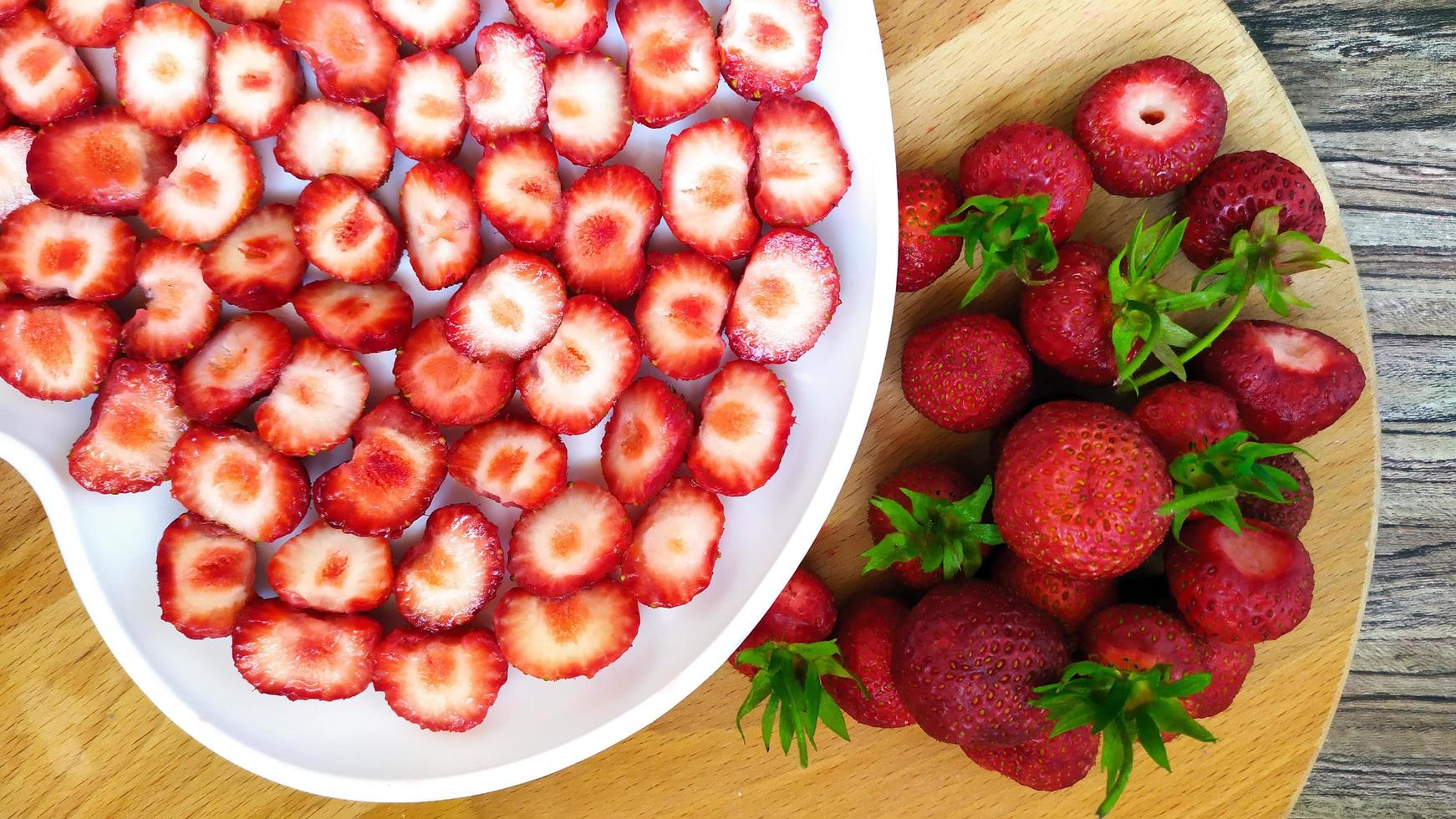 Erdbeeren in einem weißen Teller mit Herz neben ganzen Beeren foto