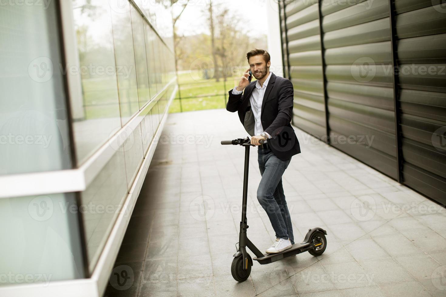 junger Geschäftsmann, der Handy auf Elektroroller benutzt foto