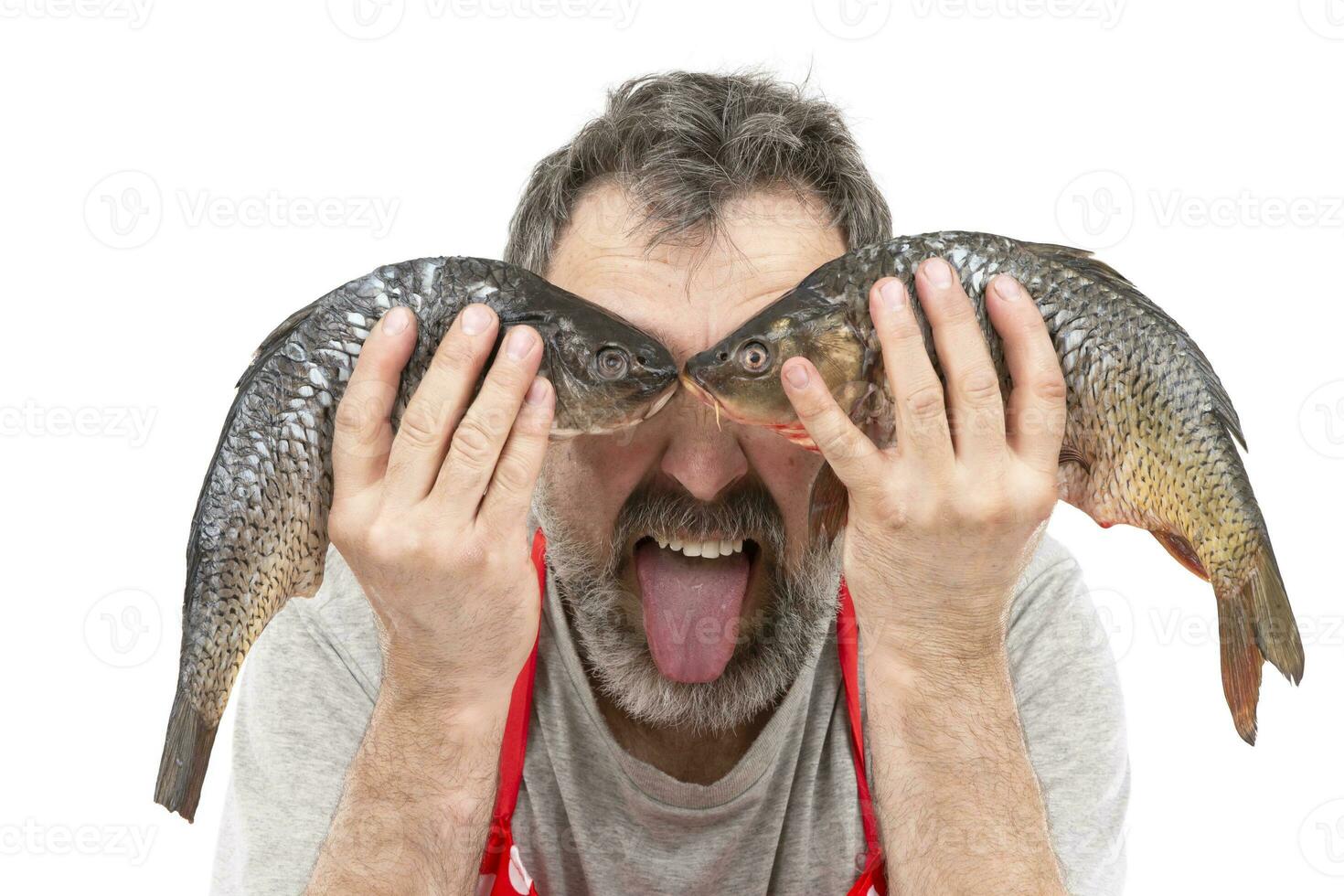 komisch bärtig Händler oder Koch halten roh frisches Wasser Fisch beim Auge Niveau und zeigen Zunge. heiter Verkäufer von das Fisch Markt. das Koch ist scherzen. foto