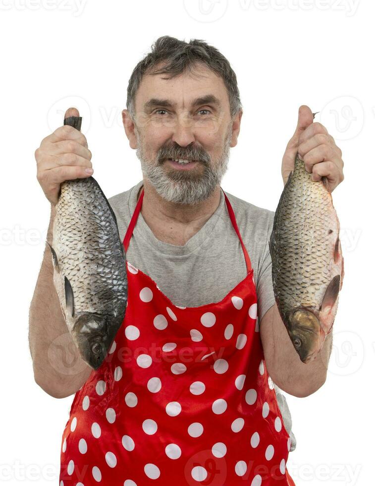 reifen Fischhändler im rot Schürze halten groß frisches Wasser Fisch und suchen beim Kamera auf Weiß Hintergrund foto