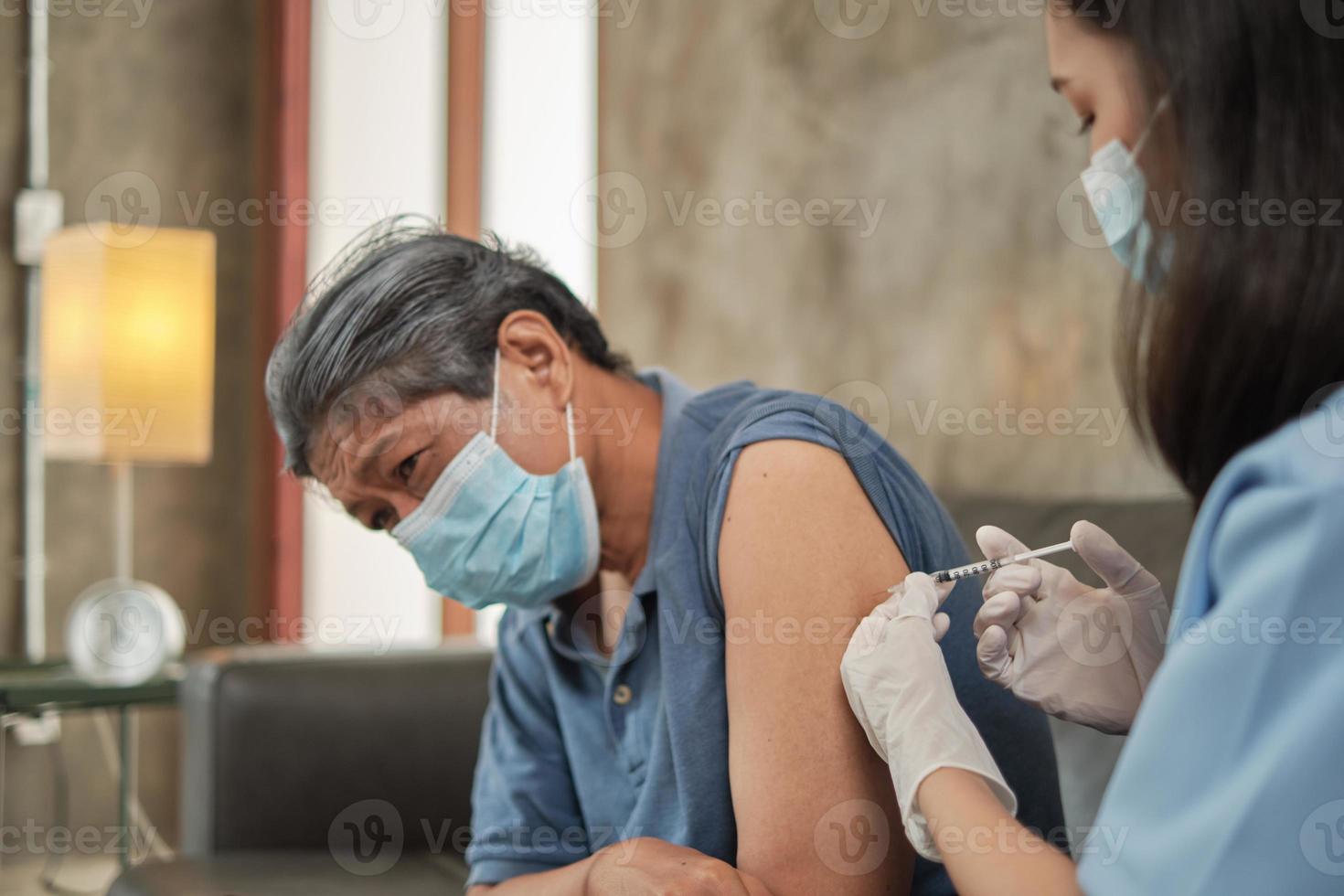 Eine asiatische Ärztin impft zu Hause einen älteren Mann. foto
