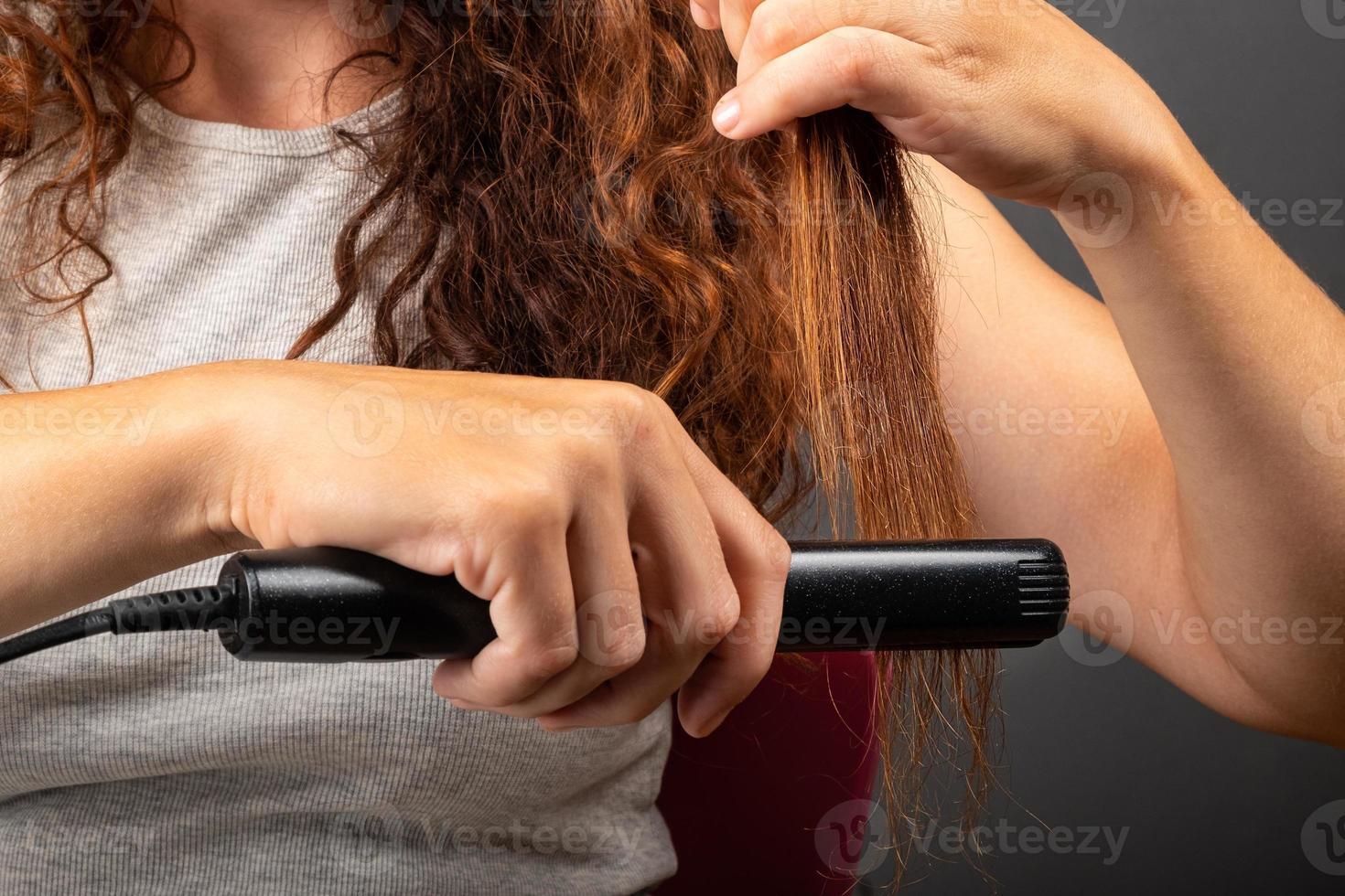 Mädchen glättet lockiges Haar mit einem Haarglätter, Lockenstab. foto