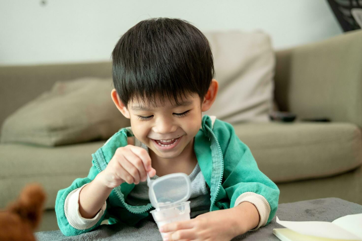 ein Junge glücklich Verwendet ein Löffel zu Scoop oben Joghurt. foto