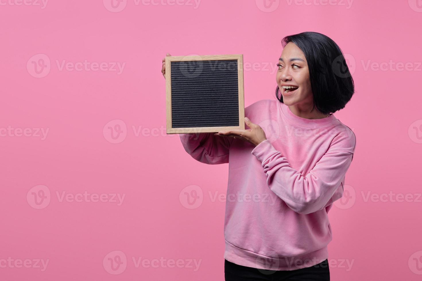 Porträt der asiatischen Frau, die leeres Brett mit lächelndem Ausdruck betrachtet foto