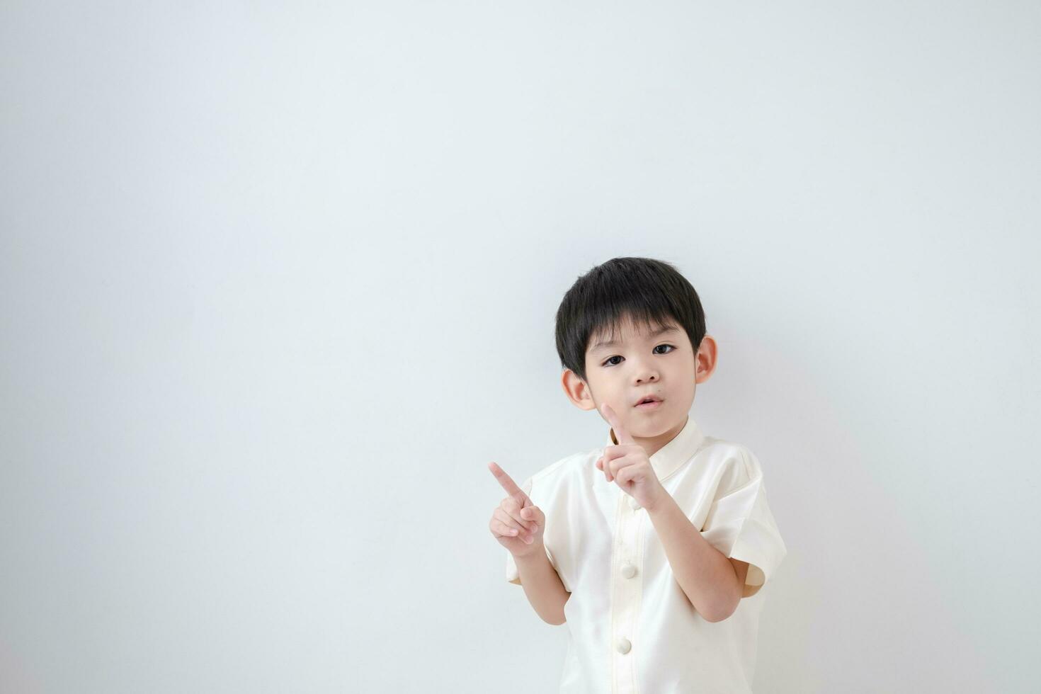 asiatisch Junge tragen traditionell thailändisch Kleidung, Stehen mit Index Finger nach oben. auf ein Weiß Hintergrund foto
