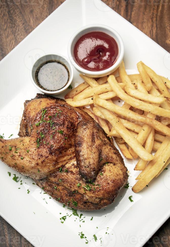 Gebratenes Drehspieß halbes Hähnchen mit Pommes Frites einfaches Essen auf weißem Teller foto