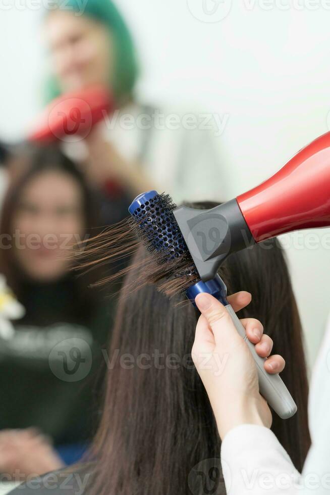 Hände von Friseur trocknet Brünette Haar von Klient mit Haar Trockner und Kamm im Schönheit Salon foto