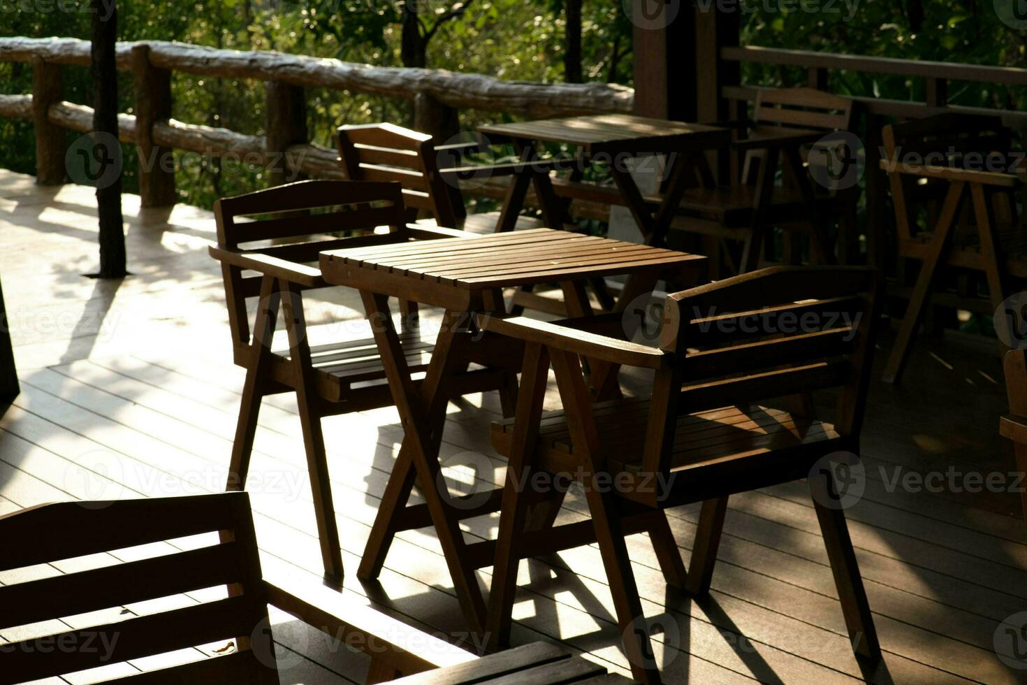 hölzern Tabellen und Stühle beim draussen Cafe Terrasse im Park. leeren Garten Möbel umgeben durch Grün Garten. foto