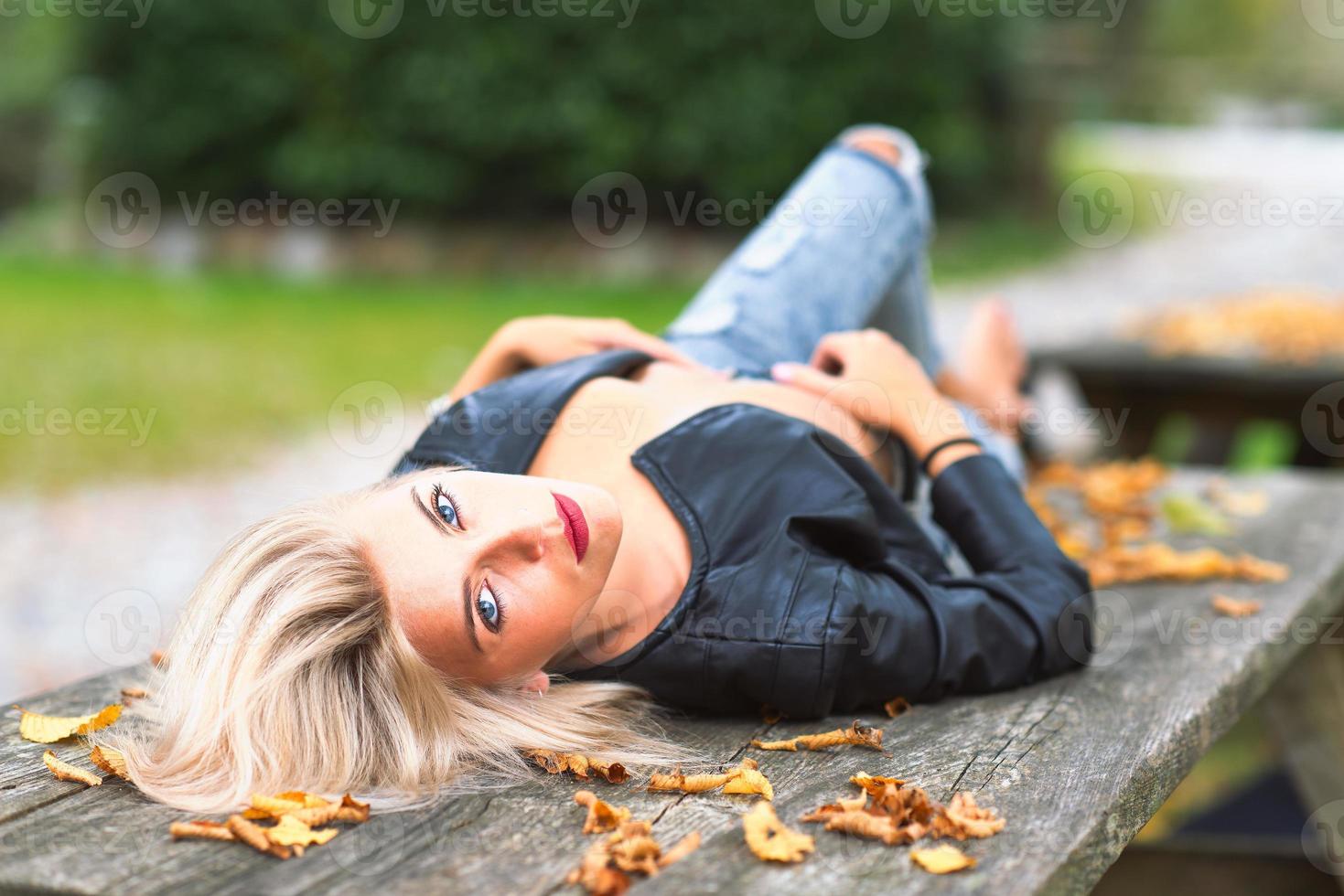 sexy blondes nacktes Mädchen, das im Herbst auf einer Holzbank liegt foto