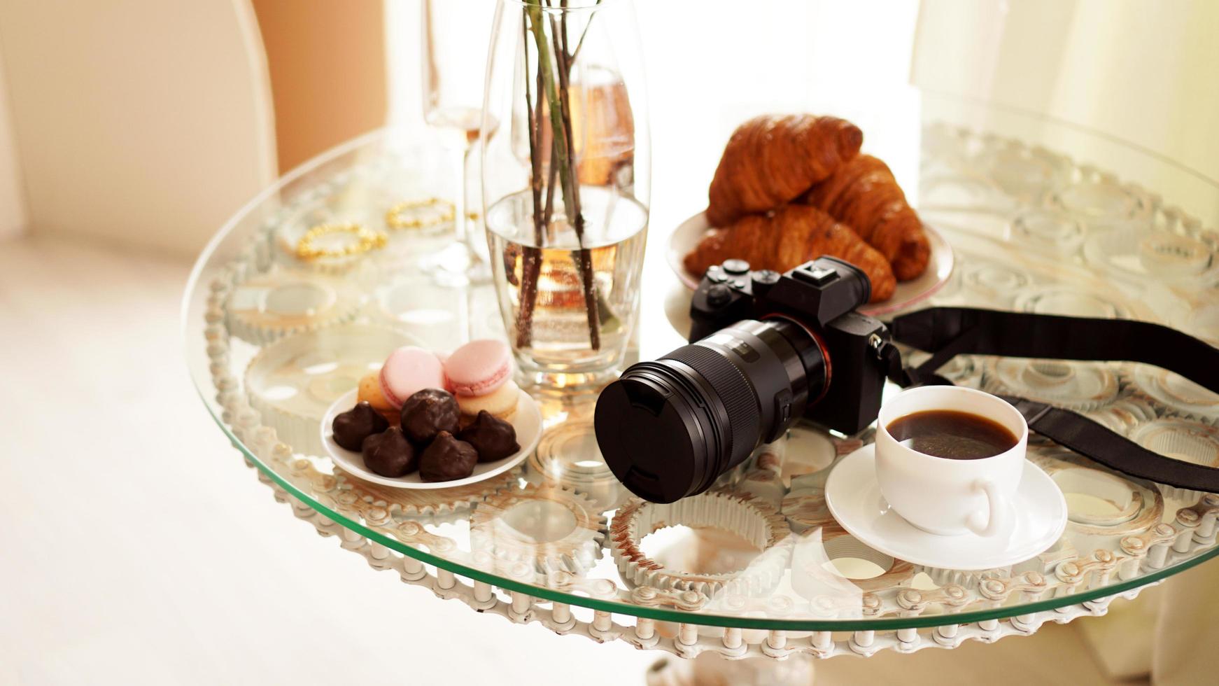 Fotokamera mit Objektiv auf Glastisch. Tasse Kaffee foto