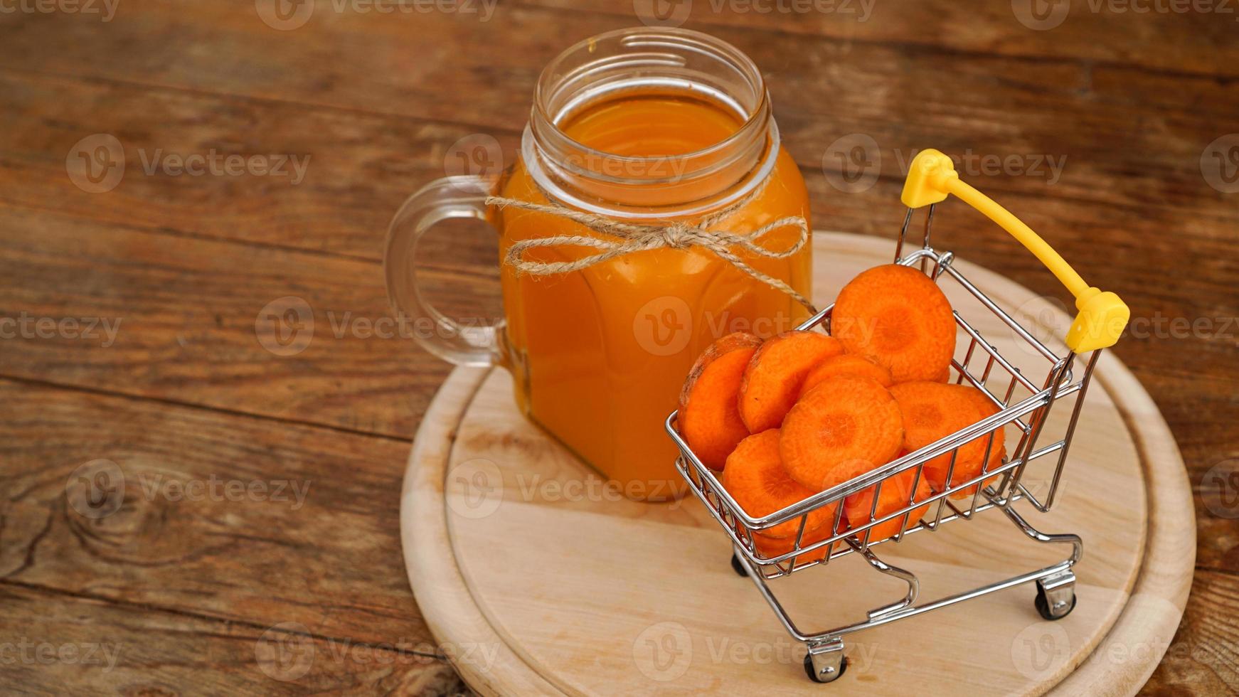 frischer Karottensaft mit Supermarktwagen und auf Holzuntergrund foto