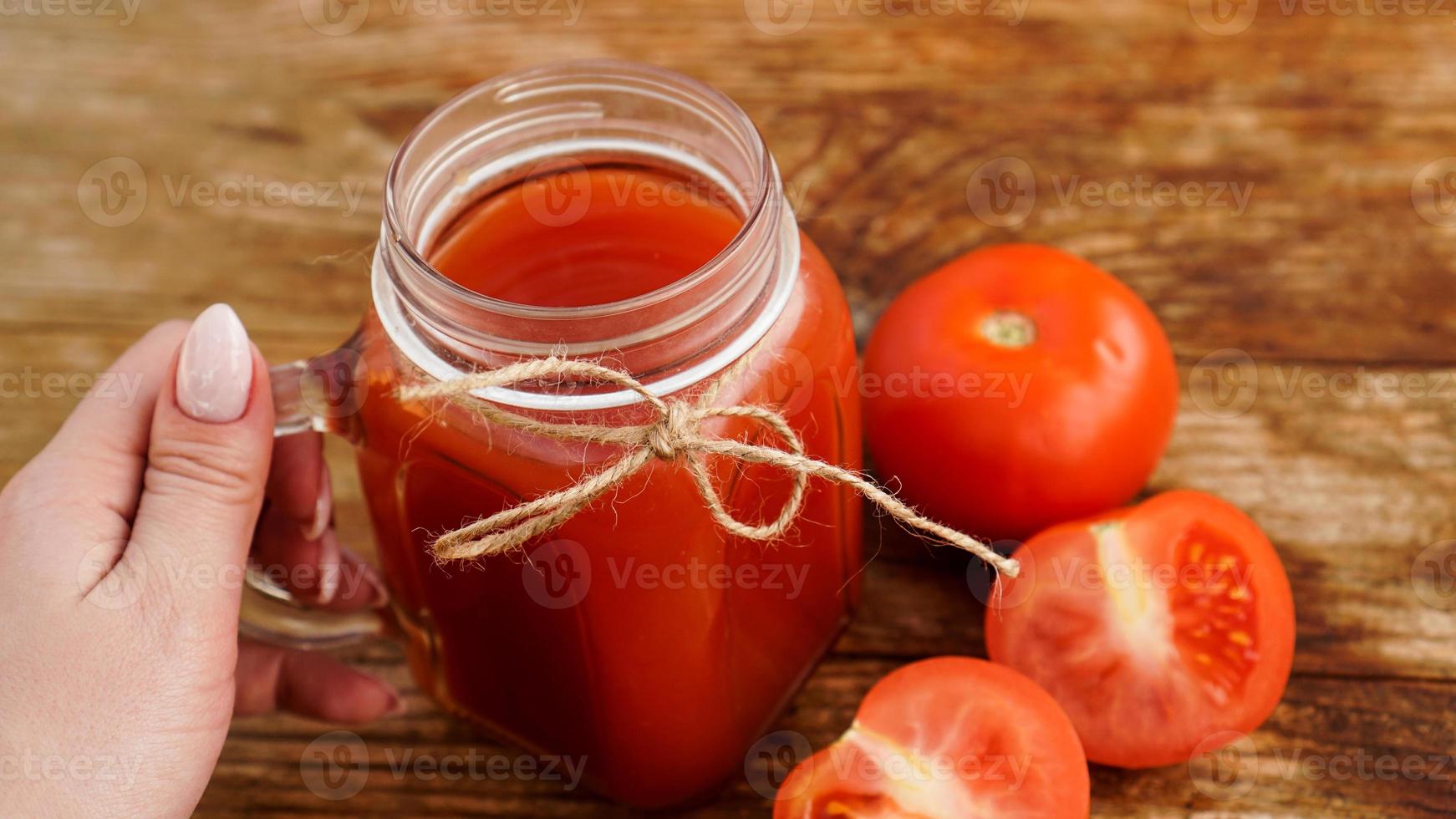 weibliche Hand hält Glas Tomatensaft auf Holztisch foto